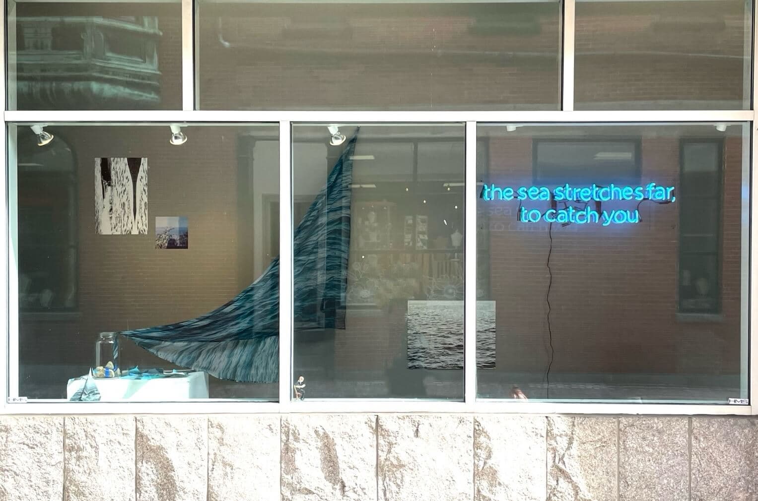 A storefront gallery boasts a neon sign and artworks that conjure the ocean.